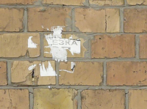 Brick fence texture made up of bricks in various shades of tan and brown, with a strip of grey cement with brick fragments near the bottom.